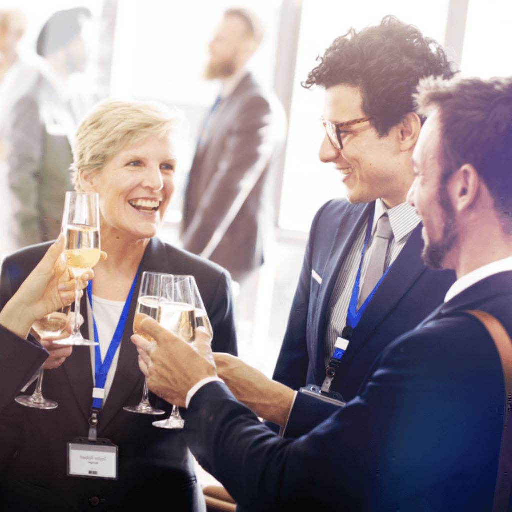 A group of professionally dressed people with ROQ Events name badges clink champagne glasses and smile at a networking event.