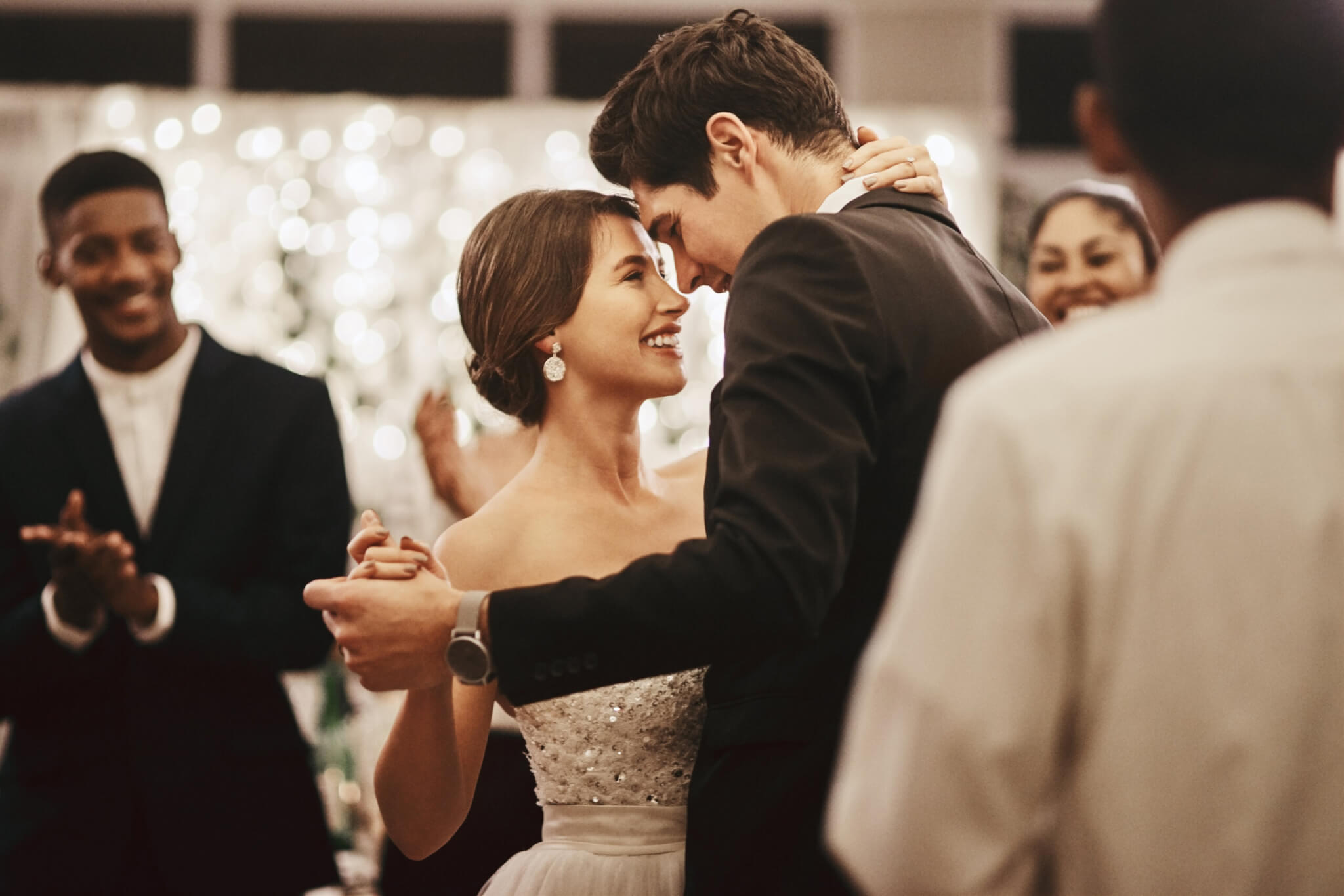 A bride and groom smile and embrace while dancing, surrounded by guests who are clapping and celebrating at a stunning ROQ Events wedding reception.